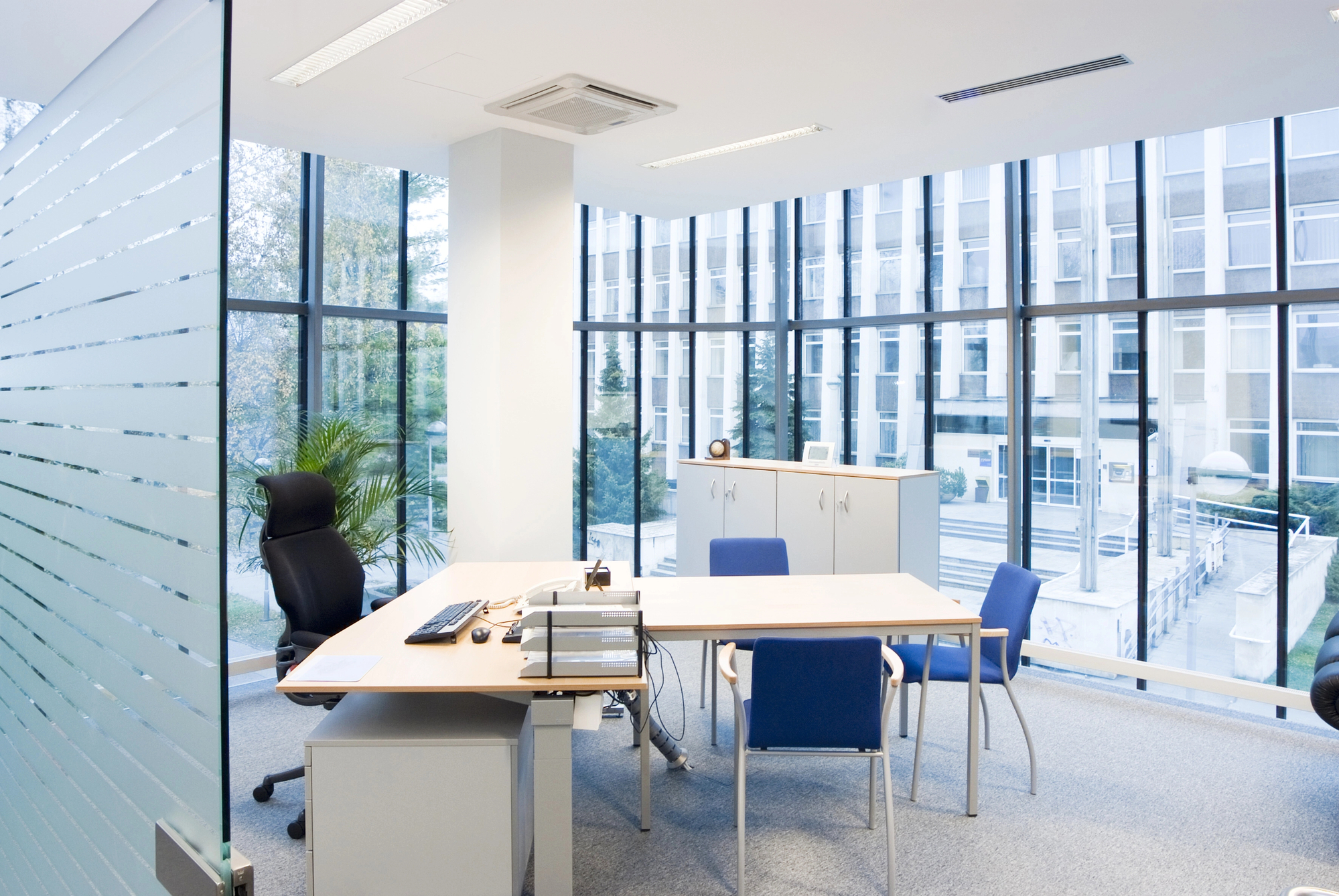 Modern office space with large windows showing smart window tint technology and minimalist furniture