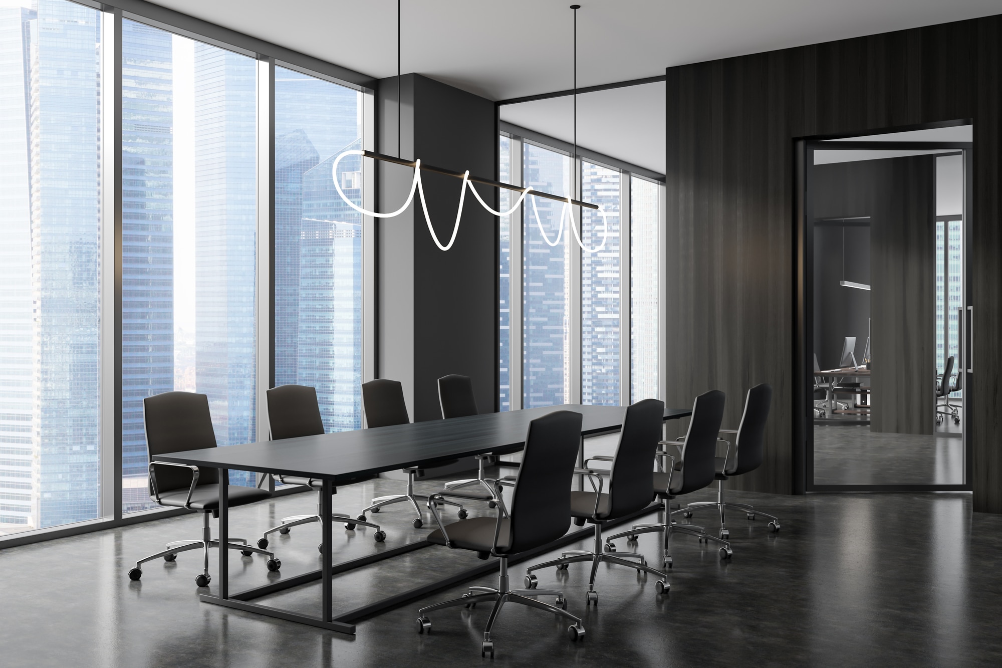 A modern conference room with a large, dark wood table, surrounded by sleek black chairs, under an artistic lighting fixture